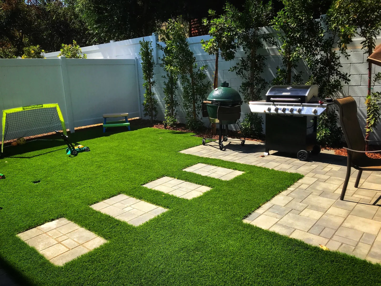 Artificial turf lawn with square stepping stones beside a paver patio