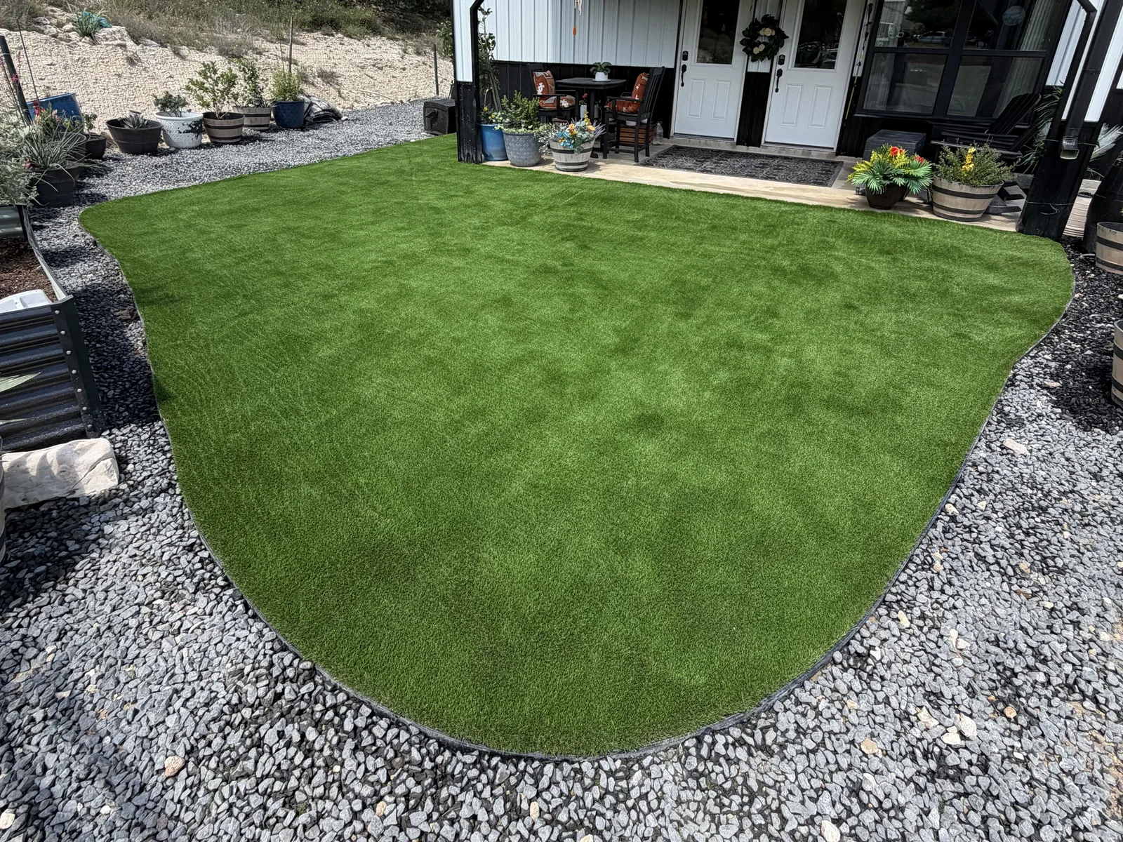 Artificial turf lawn with a curved edge and a gravel border in front of a white building