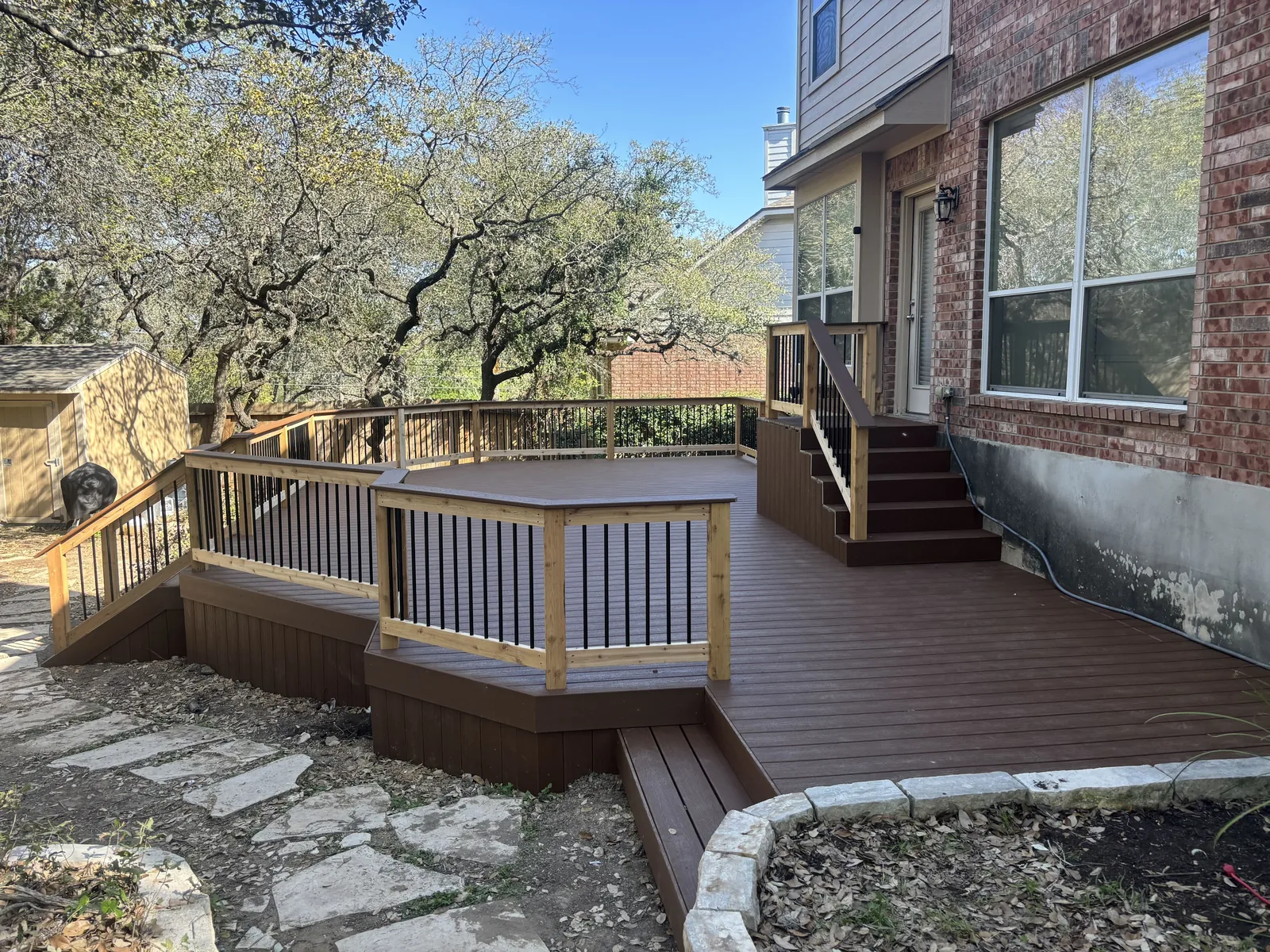 Raised composite deck with wood rails, black balusters and stairs beside a brick home