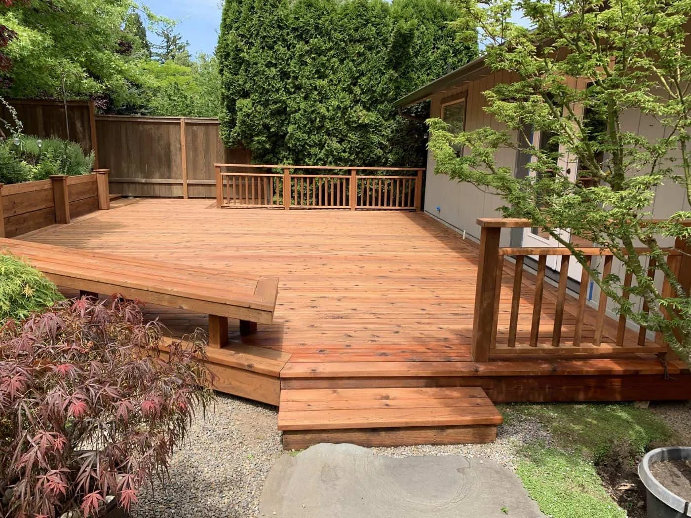 Freshly stained wood deck with steps, a bench and railings in a backyard