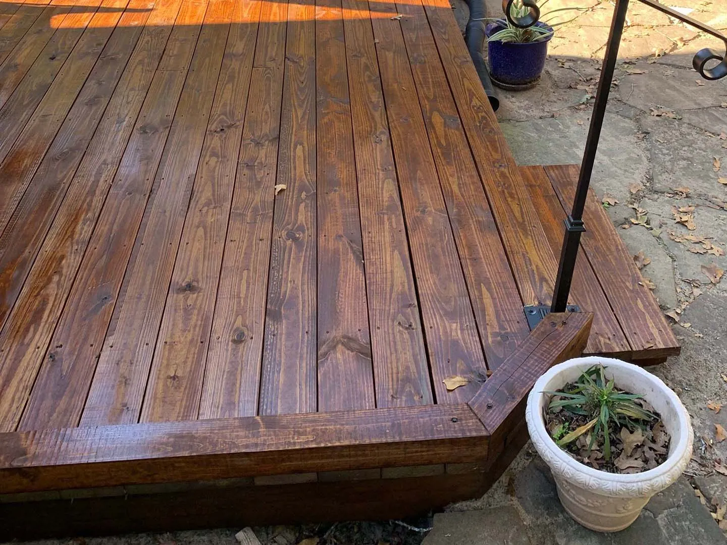 Low wood deck with a fresh coat of dark stain beside a stone patio