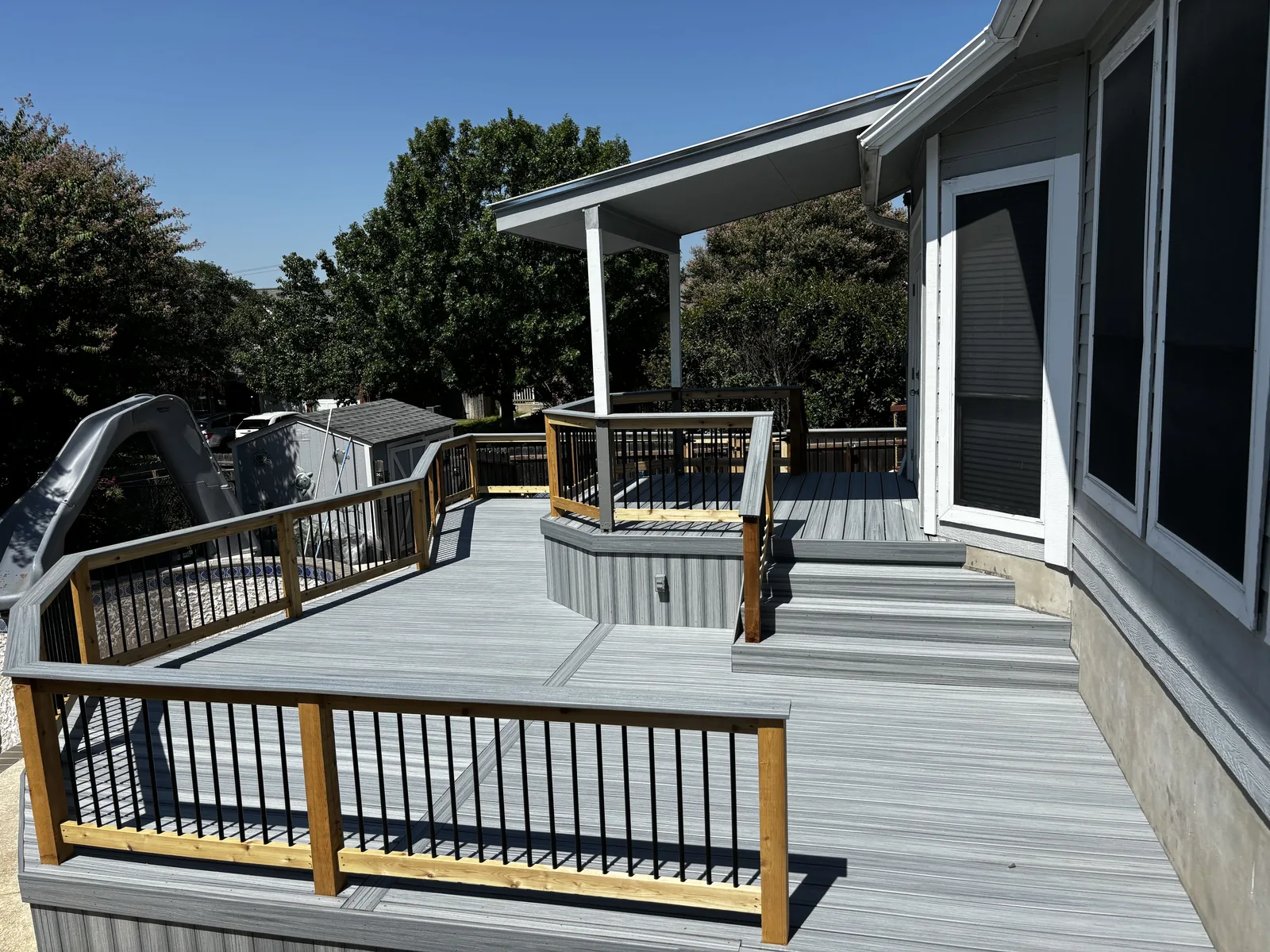 Gray composite deck with wood rails and black balusters around a house corner