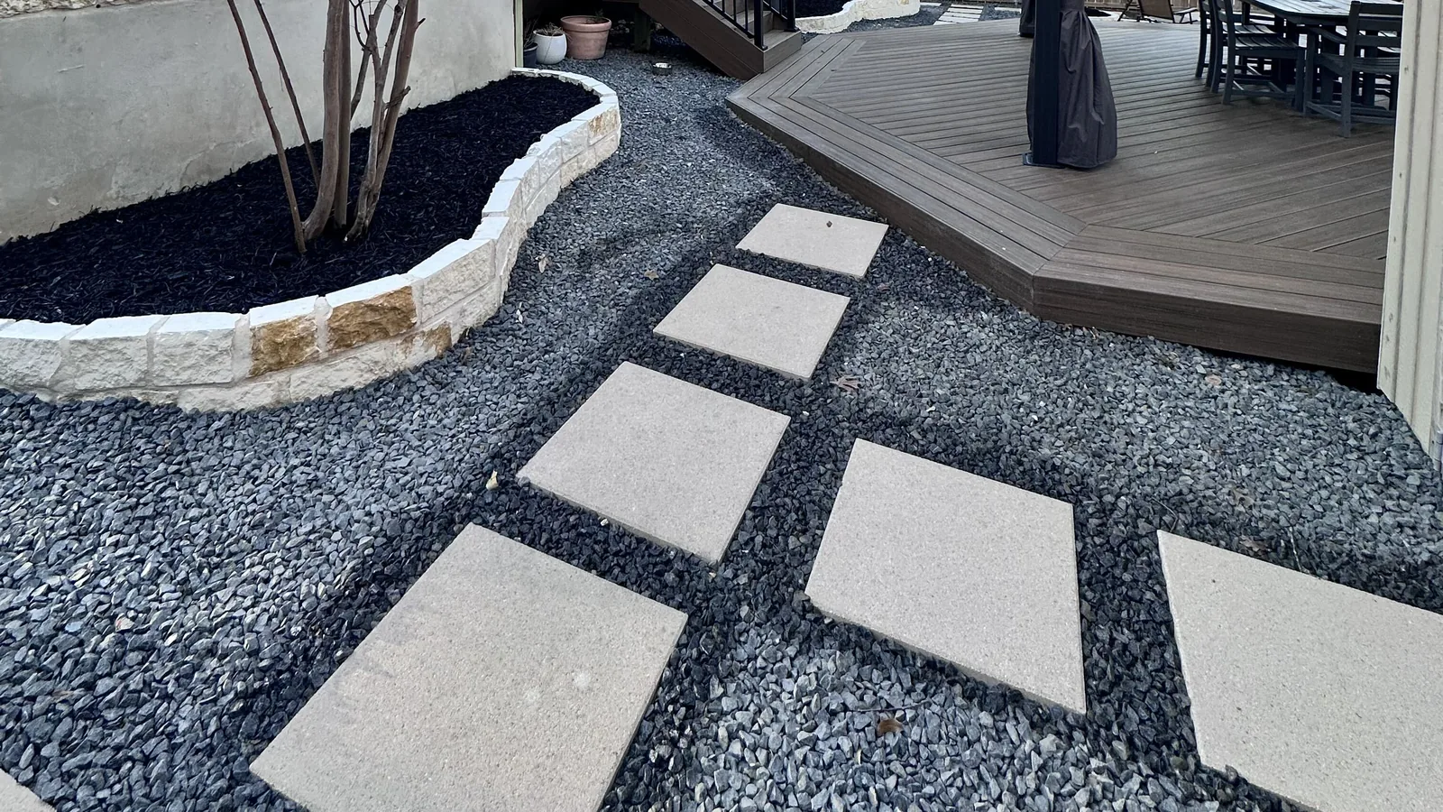 Square paver stepping stones set in gravel beside a backyard deck